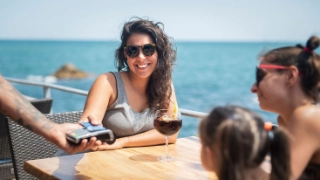 Eine junge Frau bezahlt im Ausland am Meer mit der Debit- oder Kreditkarte.